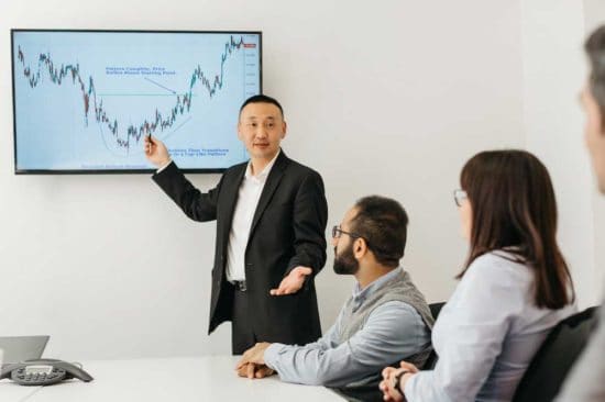 a man pointing to chart on screen in office
