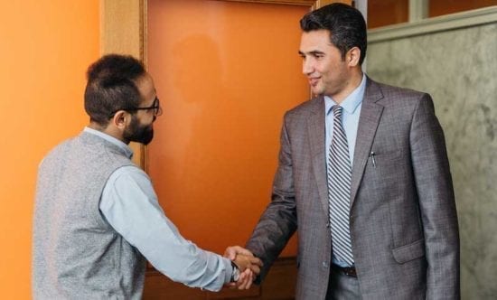 two men shaking hands in front of an orange wall