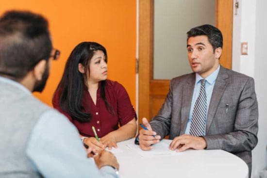 A woman and two men at a table with pens talking