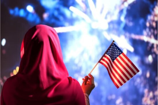 Muslim woman in a scarf holding American flag during fireworks at night